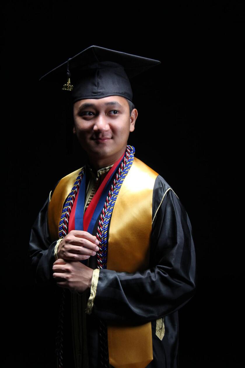 Young man stands in his black graduation gown, cap and honors.