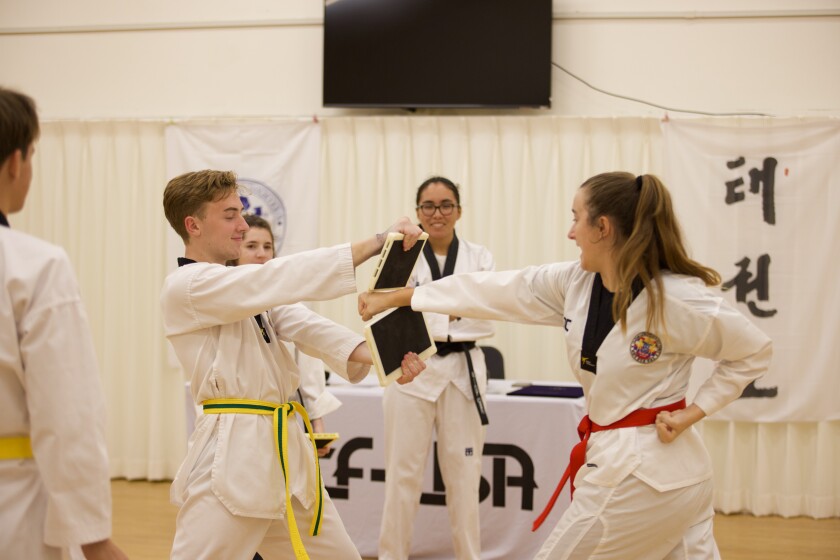 Club members gather around two students performing board breaking during a belt ceremony.