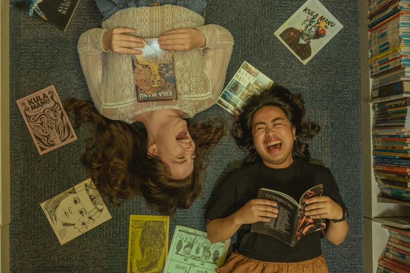 Susan Eve Suyama and Myco Marcaida laugh surrounded by copies of Kula Manu from over the years in the Smith Library
