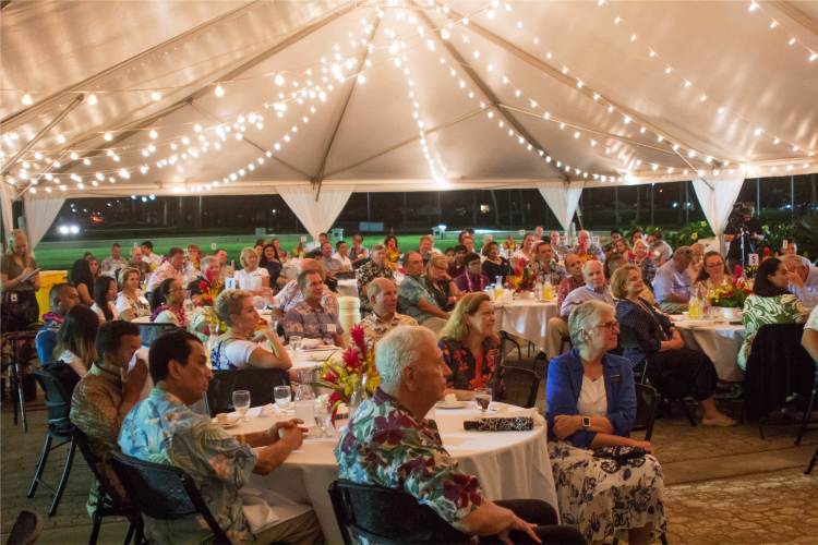 Genuine Gold society members sitting at tables under a white tent filled with lights