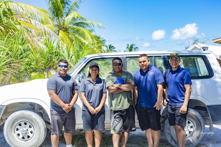 Kiribati students with their tour guide standing outside by a car.