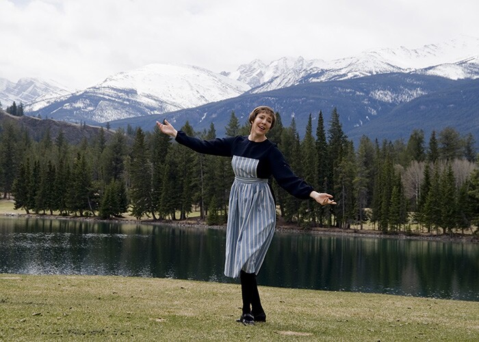a woman dressed as Maria from the Sound of Music dances in front of a lake