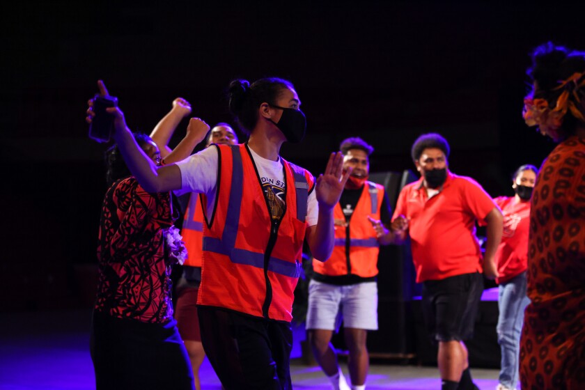 People wearing orange vests dancing around in a circle with blue light around them with a black background.