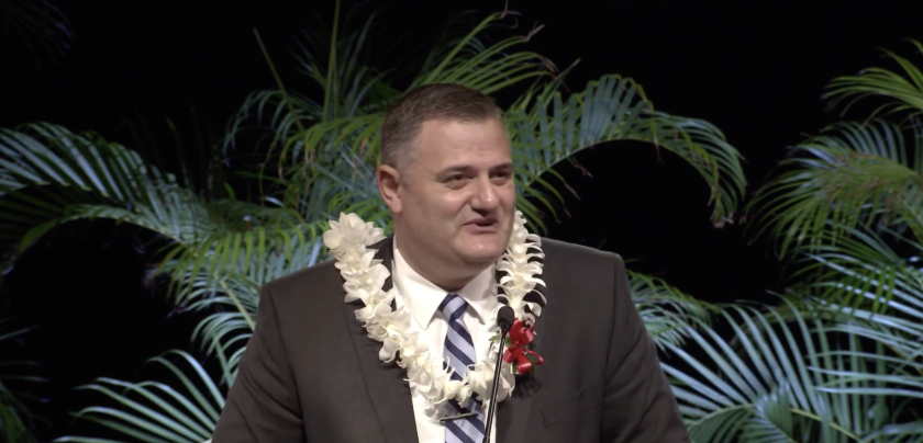 Georgi Lukov stands at the podium in a lei during the devotional