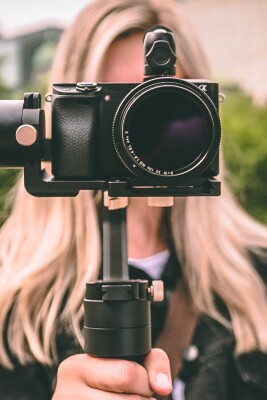 A young woman holds a camera and tripod in front of her face while filming.
