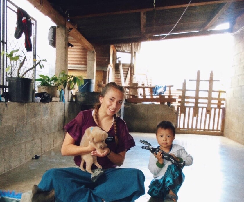 Sister Payne sitting with puppy and little boy in a house in Guatemala.