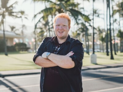 Logan Taggart stands in front of palm trees with his arms crossed