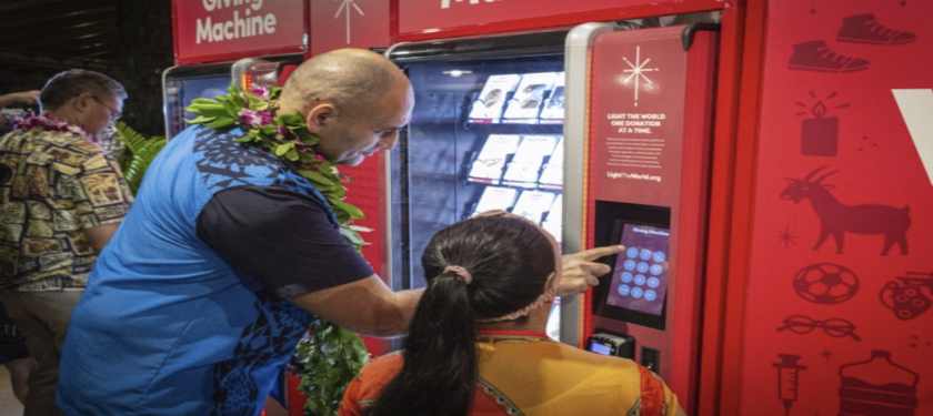 A man stands next to a girl and uses the red Giving Machine to make a donation.