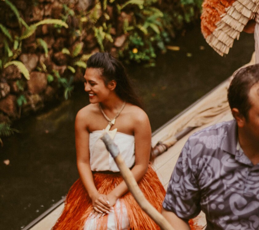 woman smiles while wearing traditional Polynesian clothes while sitting on a canoe.