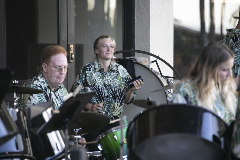 Band members, wearing green-leafed shirts, are playing on steel drums.