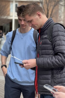 Two young men stand side by side, reading a pamphlet