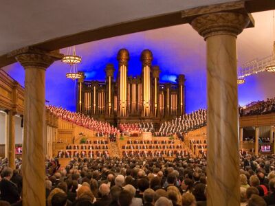 A view from the back of the Salt Lake Tabernacle interior, with people sitting on benches.