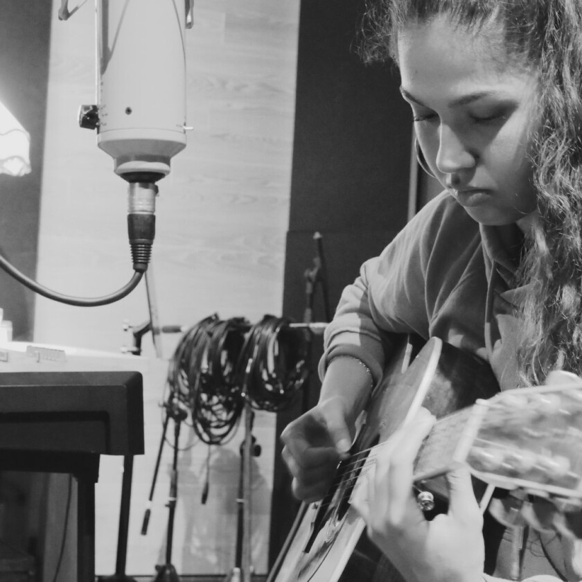 A close-up black and white photo of Kyla Greening in a recording studio. She is playing the guitar.