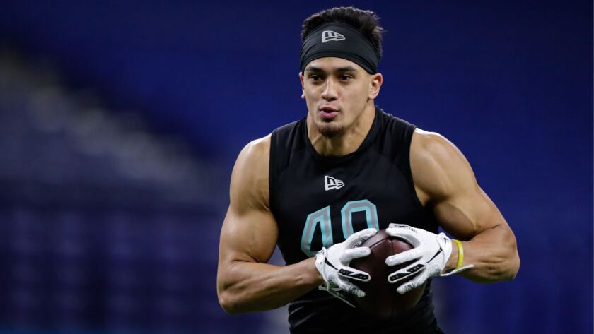 Alohi Gilman holds a football on a football field during training.