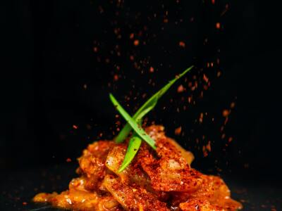 Kimchi on a black background with green vegetables on top and spices falling down onto the meal.
