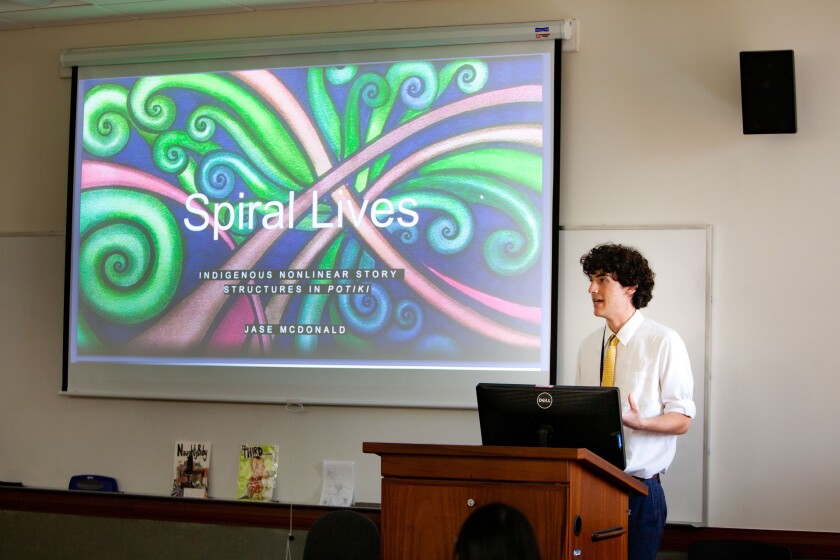 Student presenting at the URC. Slide show reads, "Spiral Lives, Indigenous nonlinear story structure in potiki, Jase McDonald."