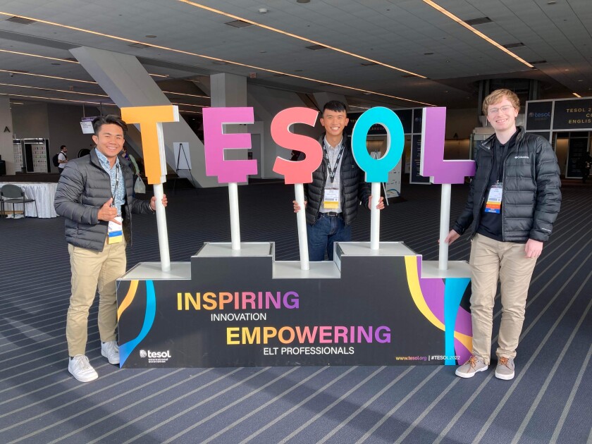 Three BYU-Hawaii students stand by a TESOL sign at the national convention in Pittsburg during Winter Semester 2022.