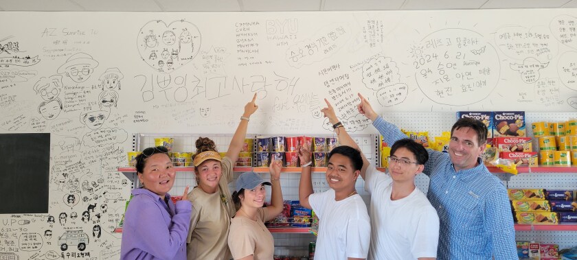 HTM Students point to the words "BYU–Hawaii HTM" written on a wall.
