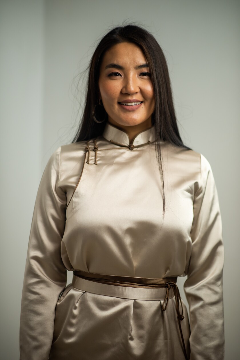 Davaasuren Myagmarjav smiling wearing an off-white silk dress with brown ties on it.