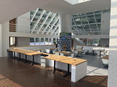 The National Humanities Center cafeteria, with tables, a podium, stacks of books on a ledge, and wide, double story windows.
