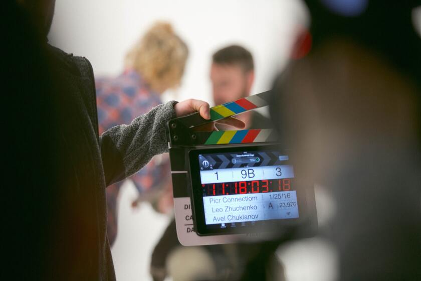 A digital director's scene board is held by a person with two actors in the background.