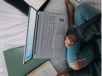 A person studying with books and a laptop on a bed.