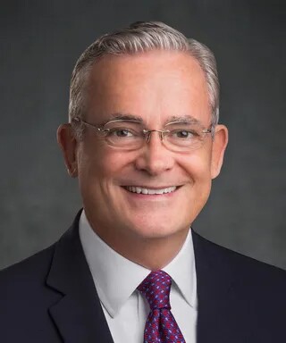 Elder Patrick Kearon wears a dark suit, white shirt and red tie.