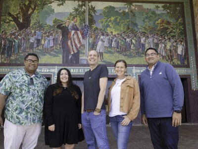 Five people pose and smile at the camera is a mosaic mural behind them.