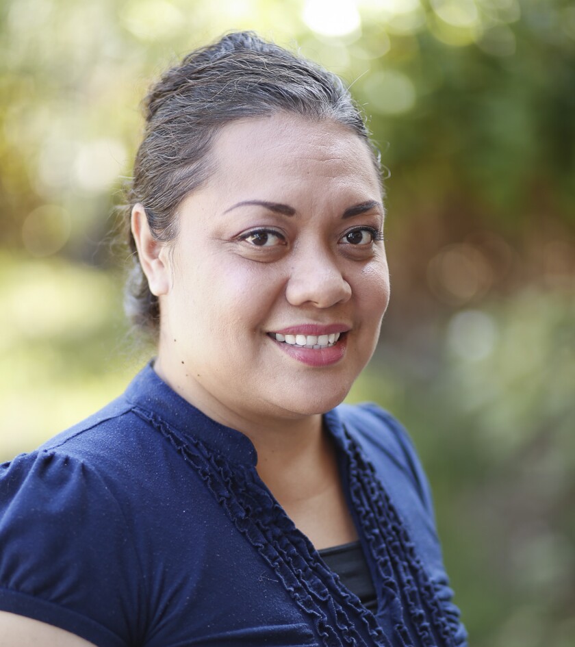 Olivia Moleni smiles wearing a dark blue shirt with greenery in the background.