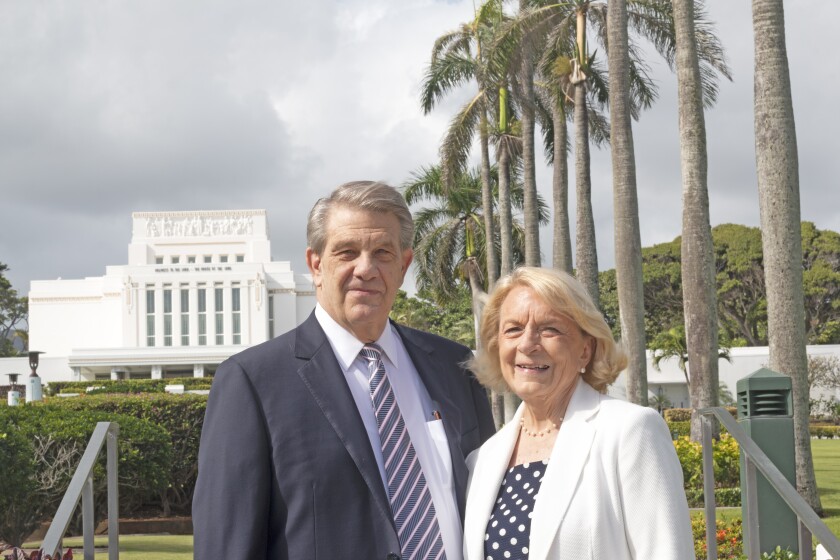 President and Sister Hallstrom smile wearing suits with the Laie Hawaii Temple and palm trees in the background.