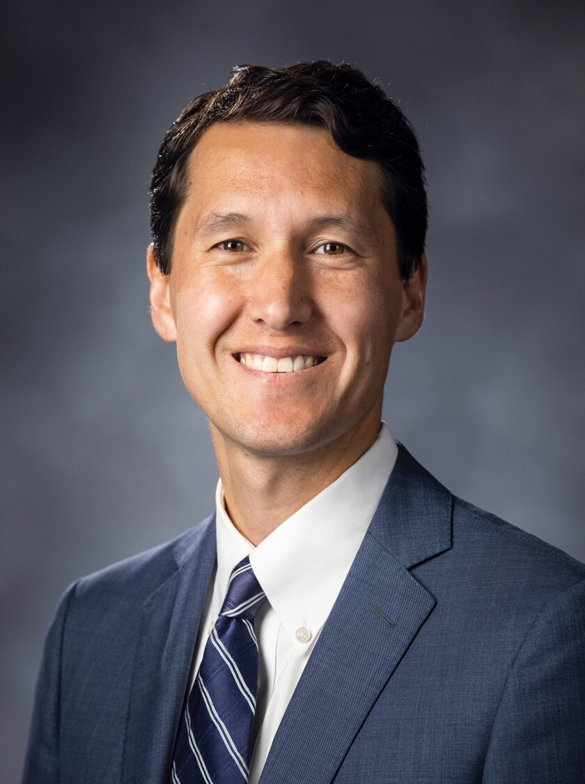A professional headshot of Isaac Smith smiling in front of a blurred gray background.