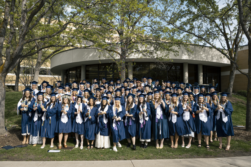 A large group of students in graduation robes pose with party poppers in hand