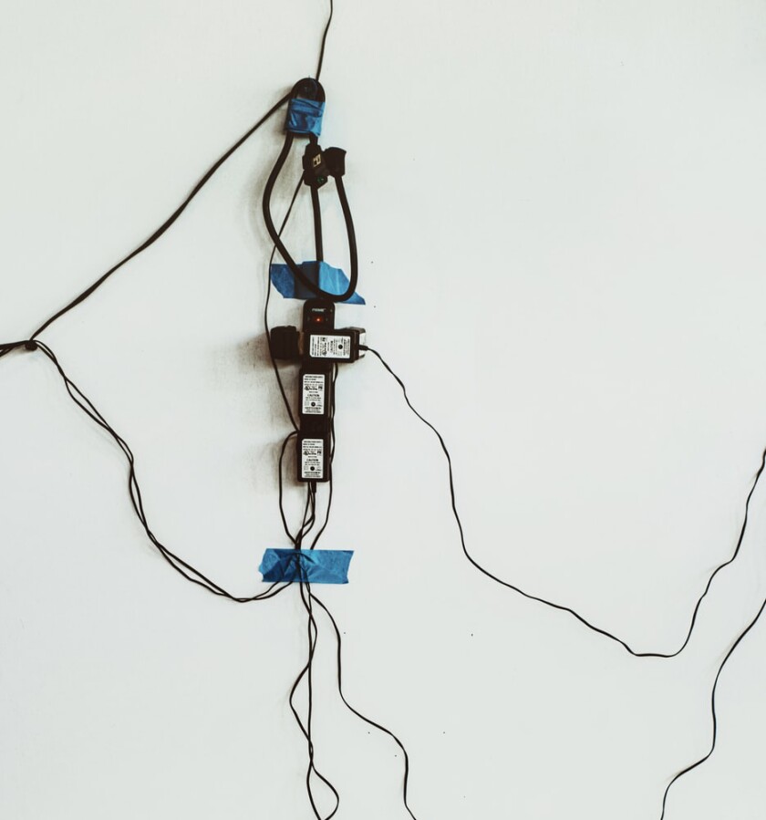 A white wall with an extension cord tied onto it with lots of cords connected to it.