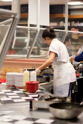 A cafeteria worker cooking food on a wok pan.
