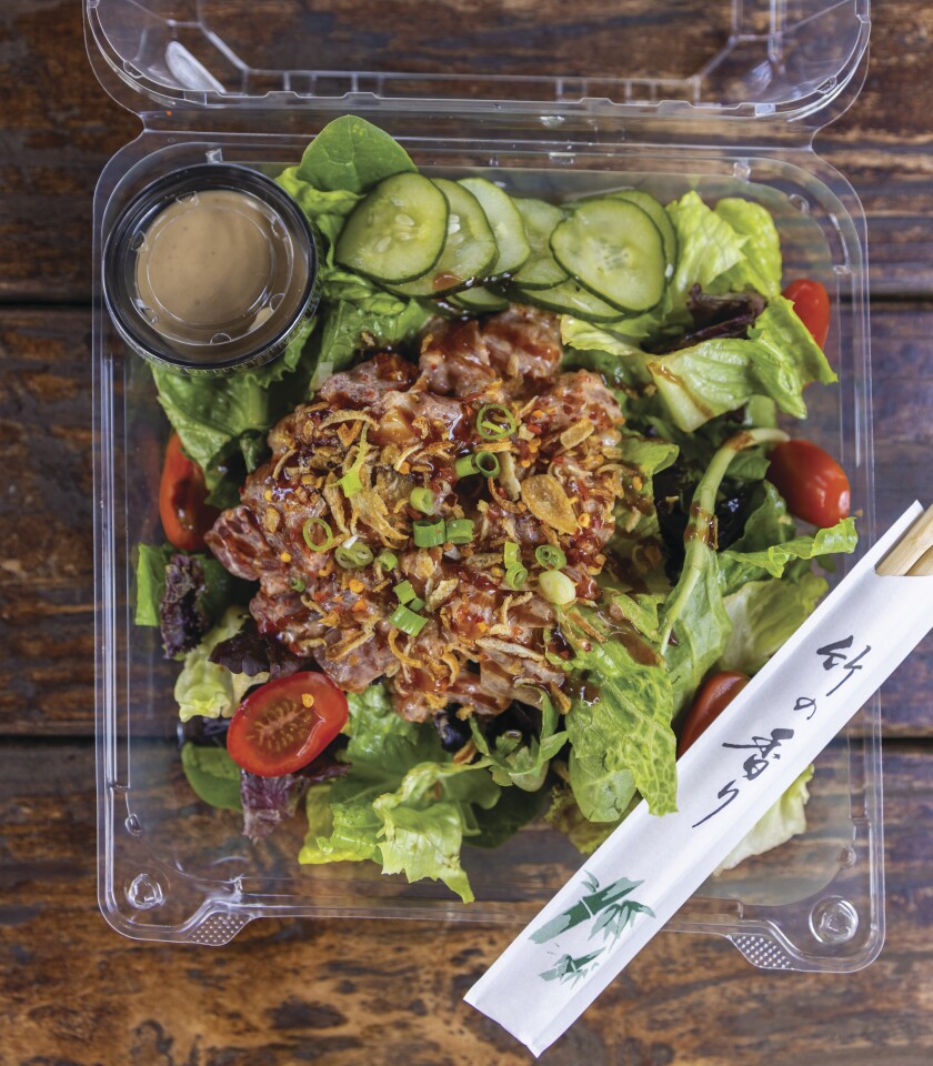 A close-up photo of a serving of poke, which is raw fish prepared with seasons and served with lettuce, cucumbers and baby tomatoes.