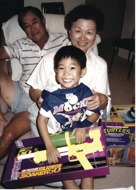 Ryan Ching's grandparents sit behind him as he opens presents of a T-shirt, Super Soaker, and Teenage Mutant Ninja Turtles toys.