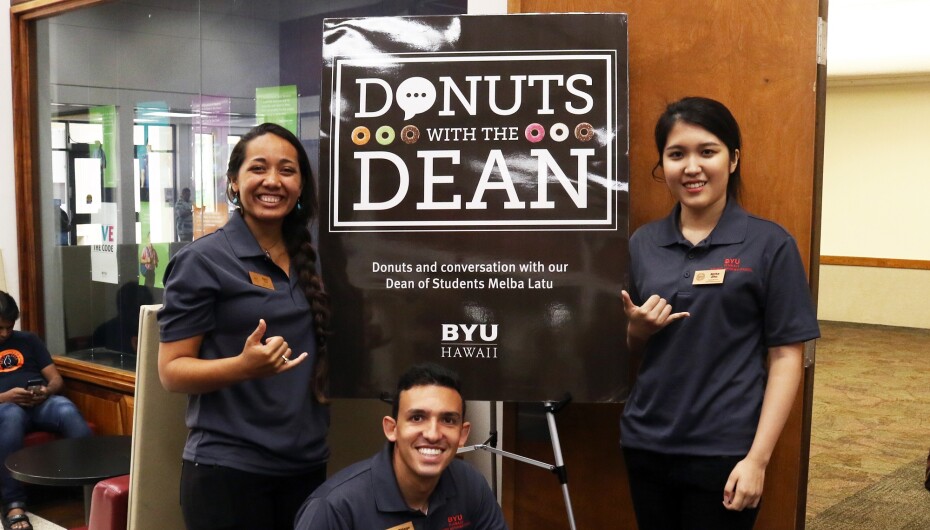3 Student Employees Standing in front of Donuts with the Dean poster