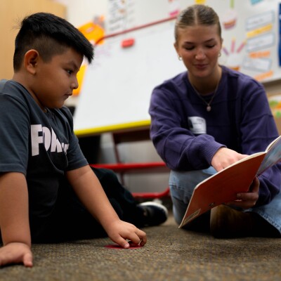 A tutor reads a book to a student.