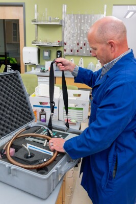 Dr. Thygerson wearing a blue lab coat takes equipment out of a case to measure samples.