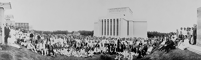 A historic black and white photograph of a large crowd of people in front of an ornate building. 