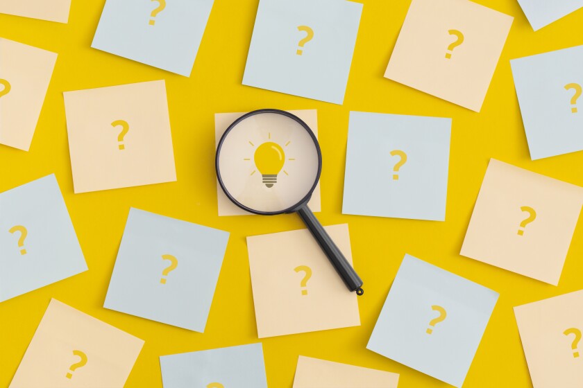 A magnifying glass hovers over a sticky note with a lit light bulb drawn on it. The other sticky notes that surround it all have question marks on them.