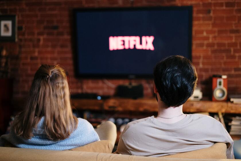 A boy and a girl on the couch with the Netflix logo on the TV.