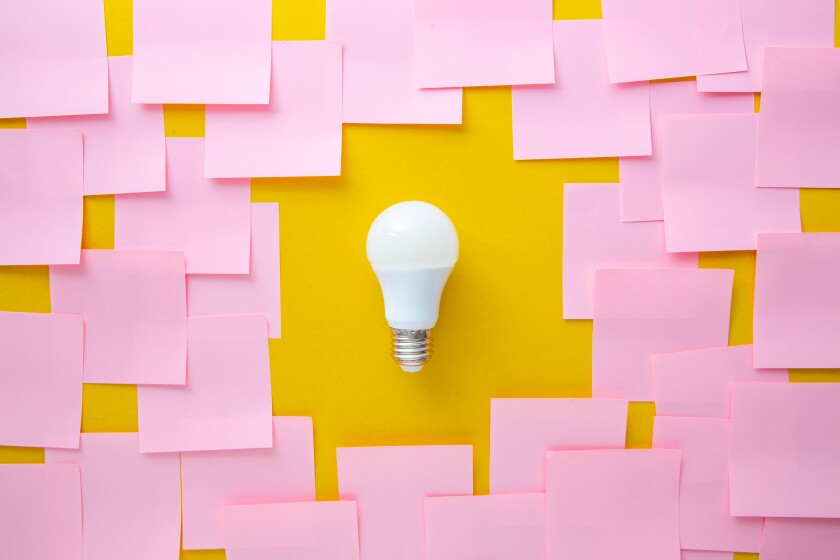 A light bulb is in the center of layered blank pink post-it notes.