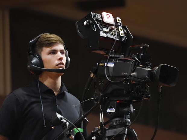 A man with headphones, monitoring behind the video camera.