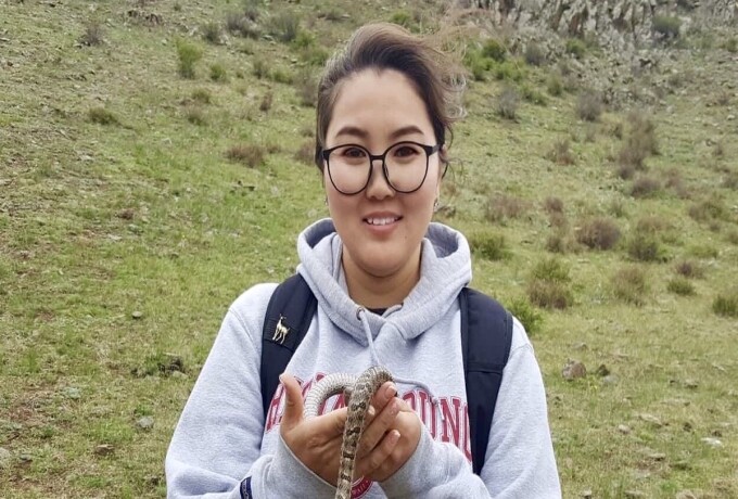 A student stands in front of a green field holding a snake