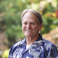 A portrait of Elder Michael King smiling at the camera with blurred green plants in the background.