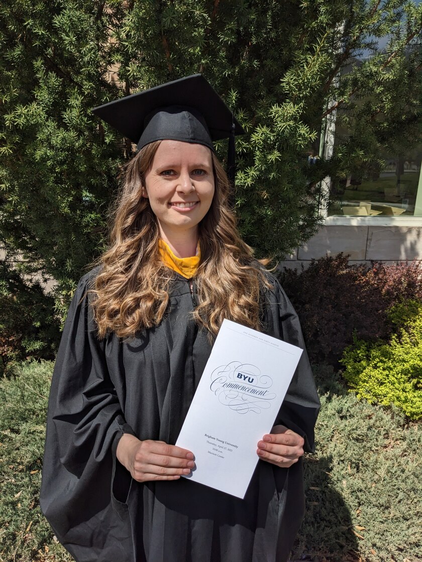 Cutler wears her graduation attire and is holding a BYU commencement pamphlet.