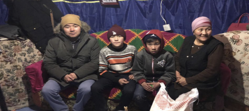 A Mongolian family sits on a couch in a house wearing winter clothing