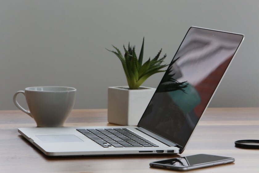 desk with laptop, smartphone, mug, and plant