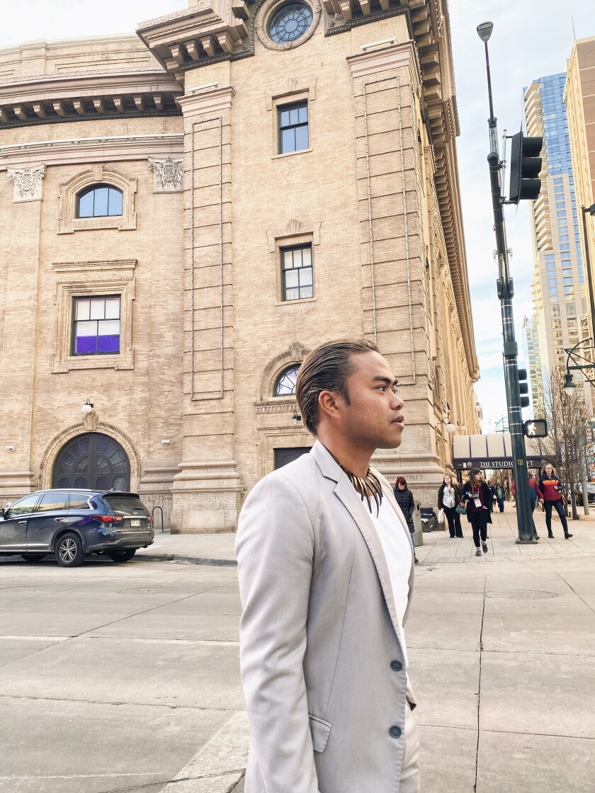 A man's profile as he walks down the street with an old brick historical building in the background.
